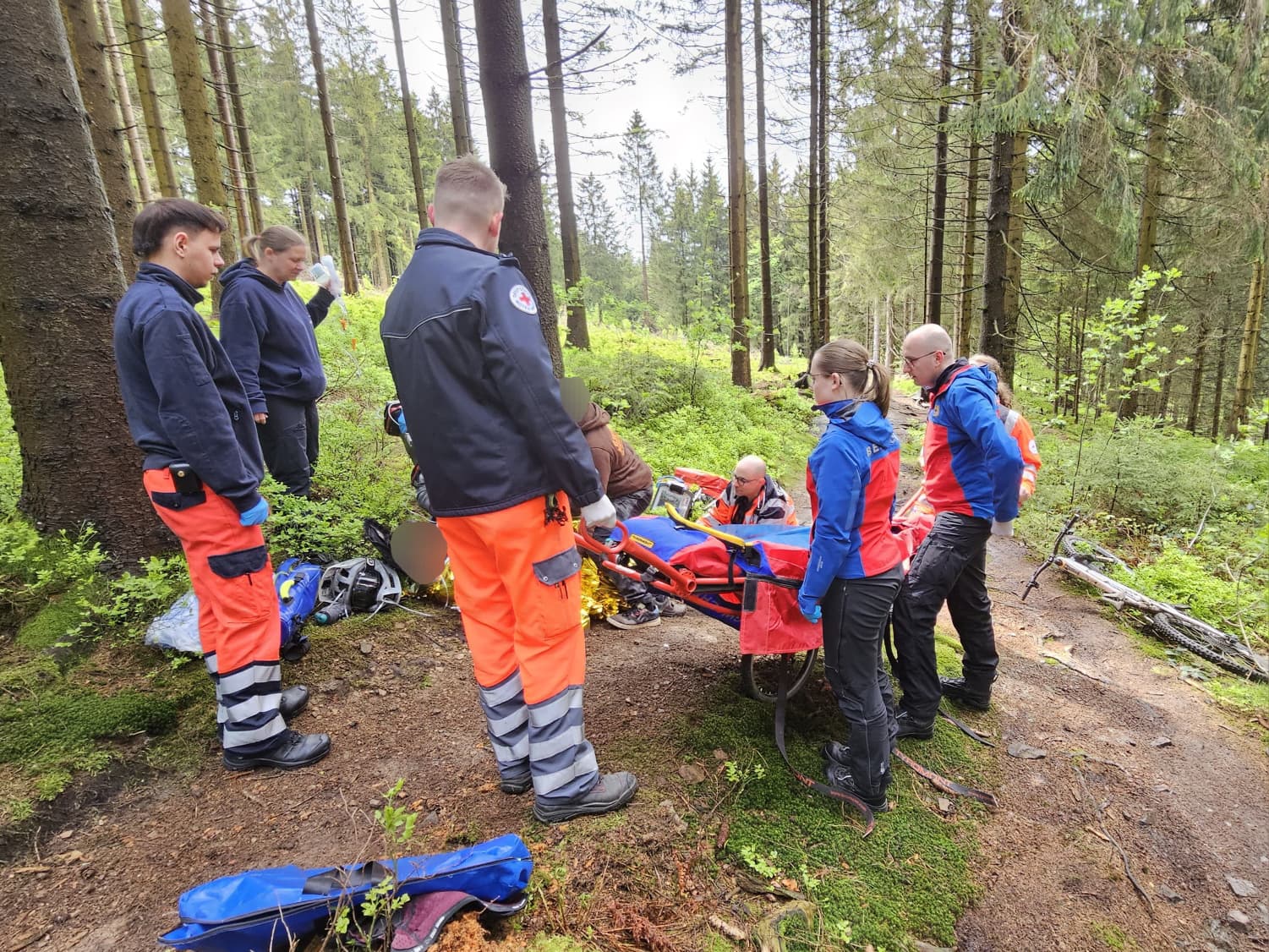 Einsatzkräfte der Bergwacht und des Rettungsdienstes versorgen einen Patienten auf einer Gebirgstrage im Wald